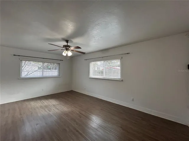 an empty room with wooden floor chandelier fan and windows