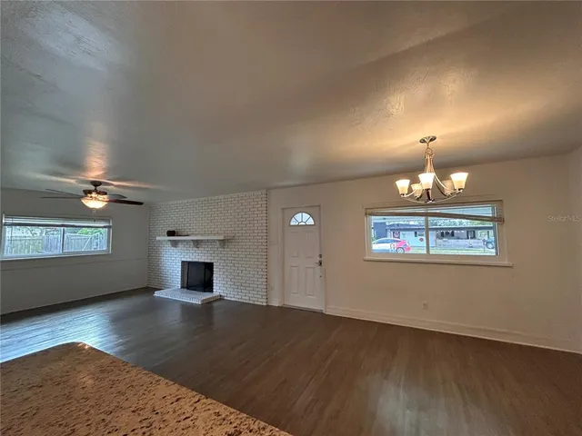an empty room with wooden floor chandelier and windows