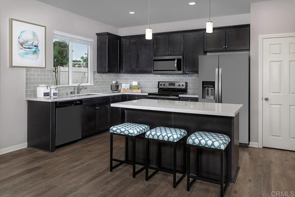 10656 Busch Street Spring Valley, CA 91978 - Photo 3 of 4 a kitchen with a refrigerator a stove a sink and a dining table with wooden floor