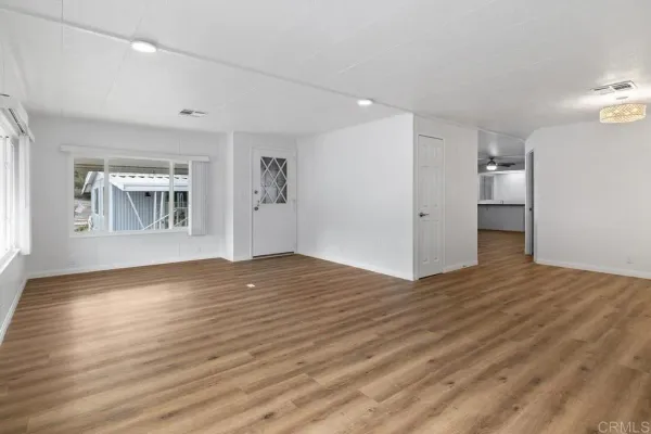 a view of empty room with wooden floor and kitchen