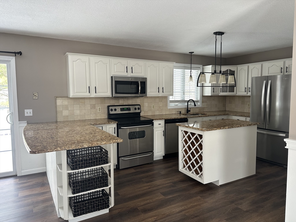 54 Old Fuller Rd Extension Chicopee, MA 01020 - Photo 9 of 25 a kitchen with kitchen island granite countertop a stove top oven a sink dishwasher a refrigerator and a dining table with wooden floor