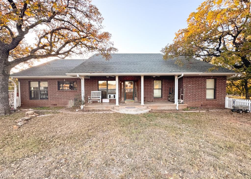 Rear view of property with a shingled roof, brick siding, and a porch