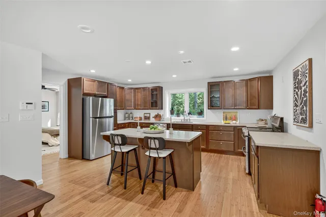 a kitchen with stainless steel appliances kitchen island granite countertop a refrigerator a stove a sink a dining table and chairs with wooden floor