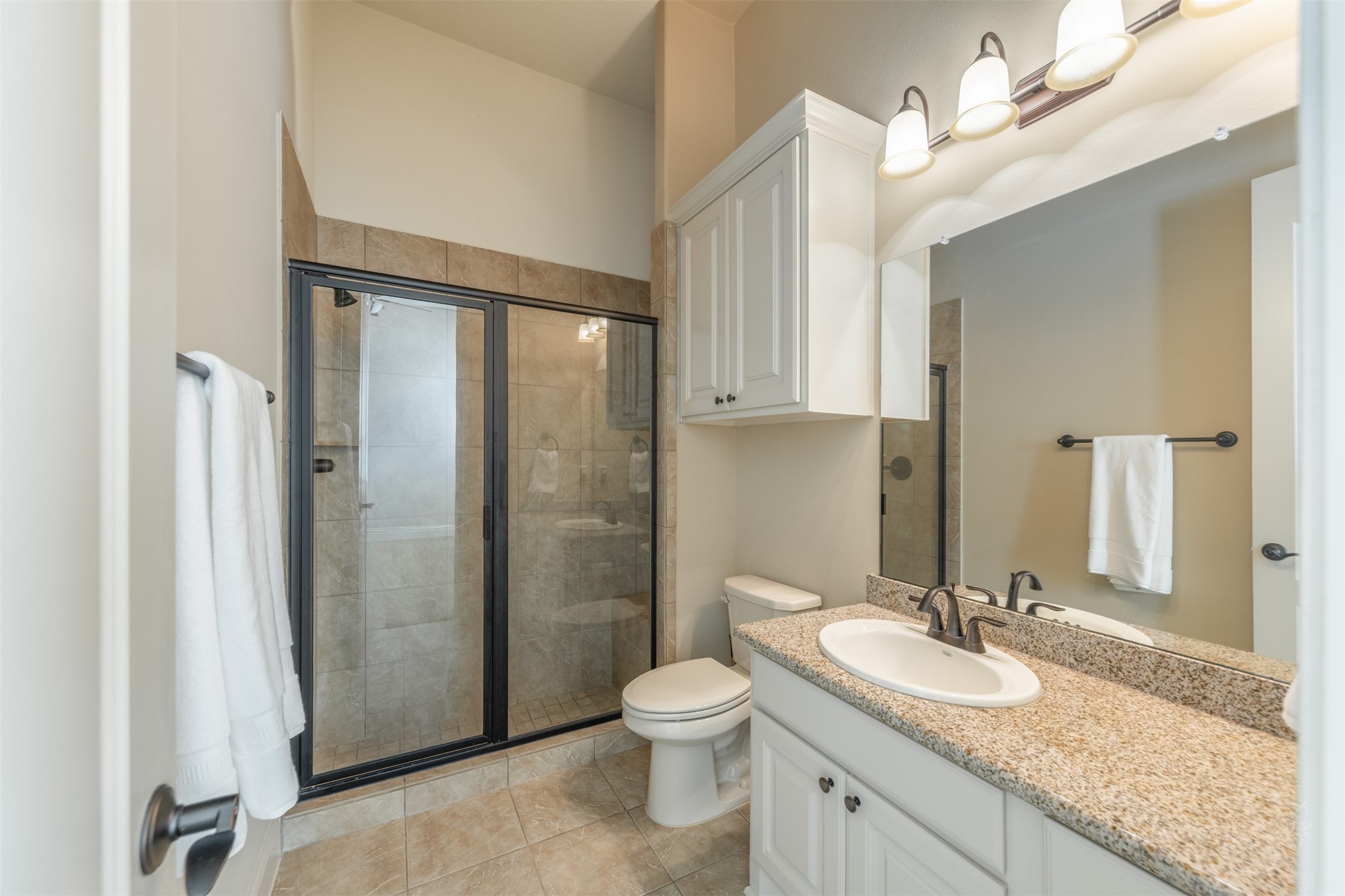 5803 Mustang Ridge Lane Fulshear, TX 77441 - Photo 21 of 48 En-suite secondary bath features granite countertops, tile flooring and a walk-in shower with glass enclosure. Thoughtfully designed finishes create a clean, timeless look for guests or everyday use.