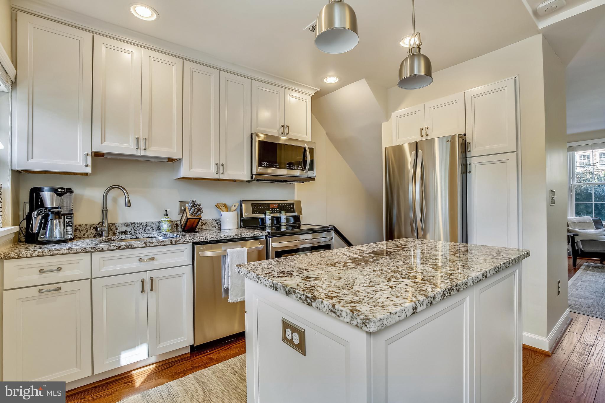 a kitchen with kitchen island granite countertop a stove a sink a refrigerator and white cabinets