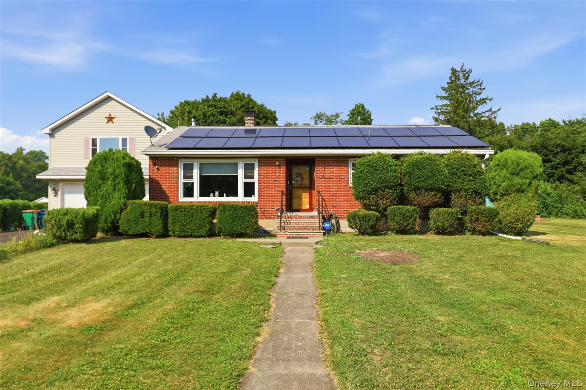 Brick facade home featuring solar panels and a landscaped front yard with a concrete walkway