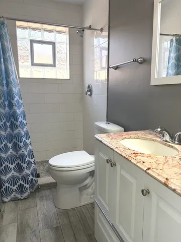 a bathroom with a granite countertop toilet a sink and a window