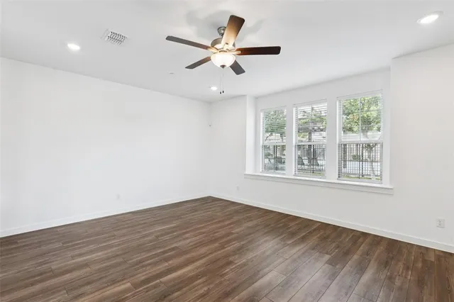an empty room with wooden floor fan and windows