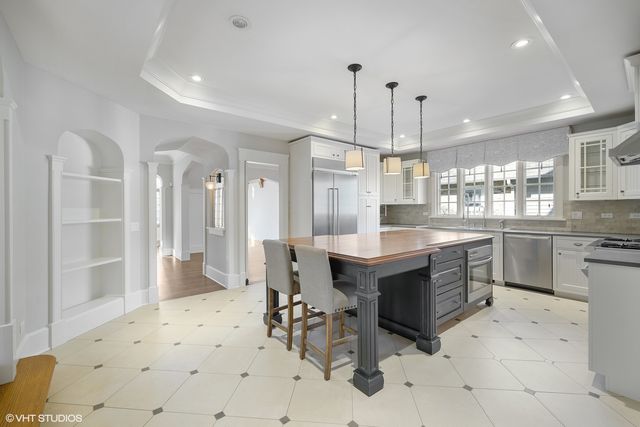 a large white kitchen with a large island in the center and stainless steel appliances