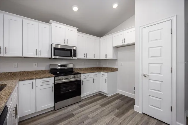 a kitchen with stainless steel appliances granite countertop grey cabinets a stove a sink and dishwasher with wooden floor