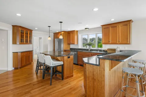 a kitchen with stainless steel appliances granite countertop a sink a stove a refrigerator and island with wooden floor