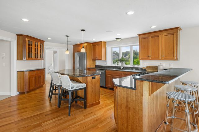 a kitchen with stainless steel appliances granite countertop a sink a stove a refrigerator and island with wooden floor