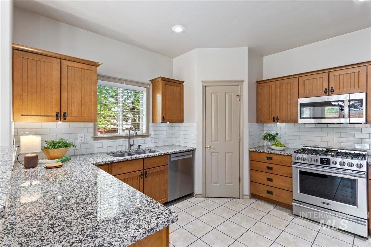 2274 Eastwood Road Twin Falls, ID 83301 - Photo 12 of 38 Kitchen featuring granite countertops, subway tile backsplash, wood cabinetry, stainless steel appliances, and tile flooring