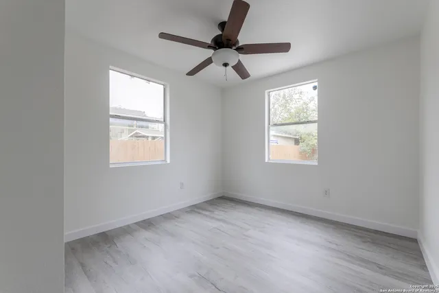 an empty room with wooden floor ceiling fan and windows