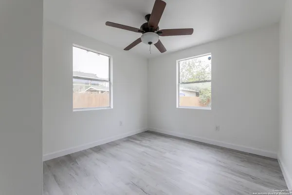 an empty room with wooden floor ceiling fan and windows