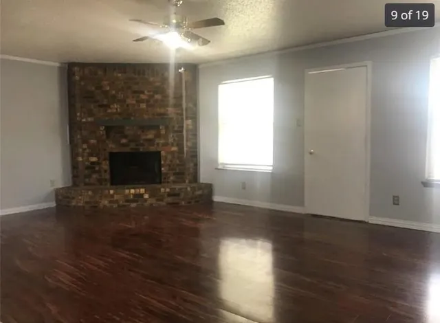 an empty room with wooden floor fireplace and windows