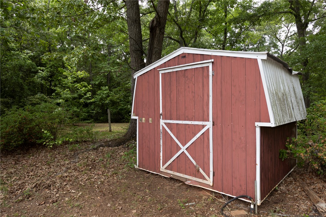 1116 Leatherdale Road Iva, SC 29655 - Photo 40 of 46 This charming red shed offers versatile outdoor storage amidst a serene, wooded landscape.