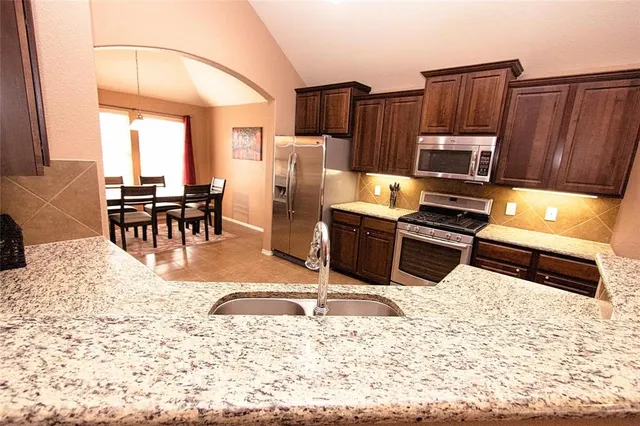 a kitchen with stainless steel appliances kitchen island granite countertop a stove a refrigerator a sink a dining table and chairs with wooden floor