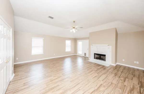 an empty room with wooden floor fireplace and windows