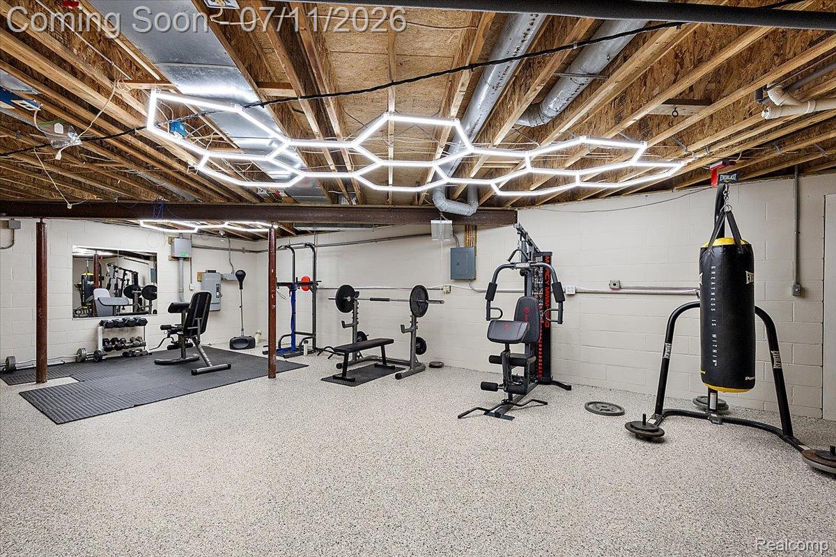 4219 Gardner Road Metamora, MI 48455 - Photo 57 of 87 Finished lower level space featuring exposed ceiling joists with modern hexagonal lighting, light-toned epoxy flooring, white painted block walls, and a large wall-mounted mirror