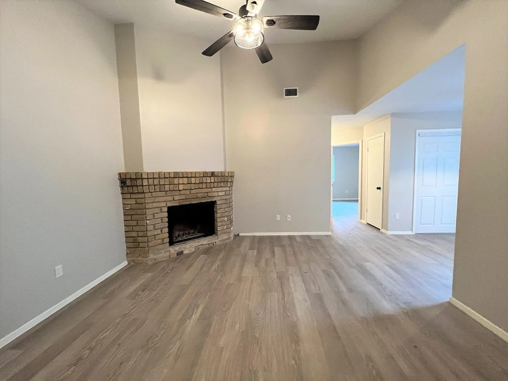 12214 Thompkins Drive, Unit B Austin, TX 78753 - Photo 4 of 13 Unfurnished living room featuring wood finished floors, a ceiling fan, a fireplace, and a high ceiling
