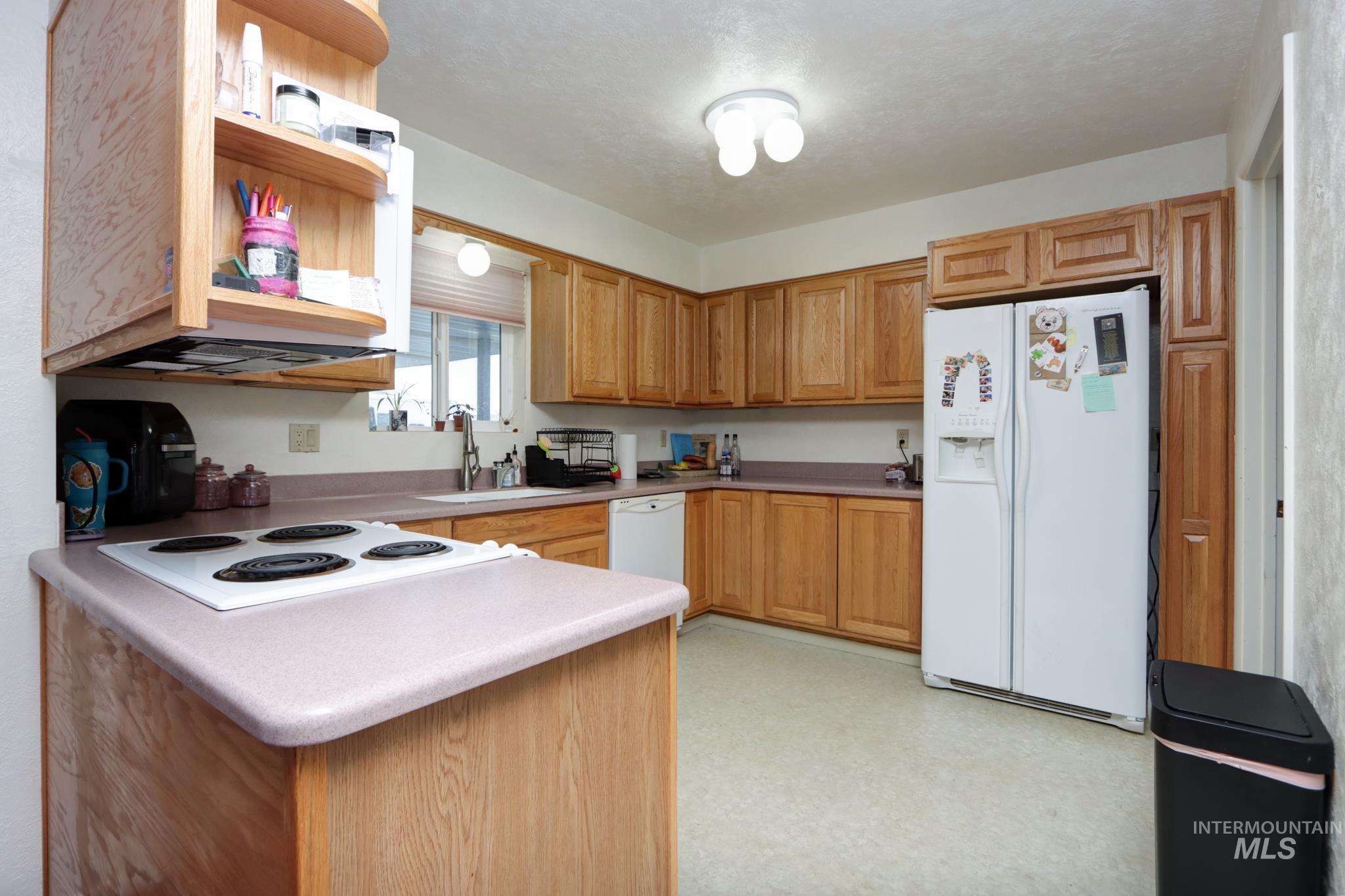 1302 Southwest 12th Street Ontario, OR 97914 - Photo 9 of 35 Kitchen with white appliances, light floors, a peninsula, wood finish cabinets, and light countertops
