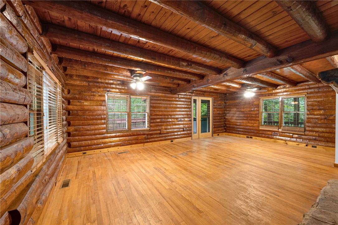 237 Spring Valley Road Liberty, SC 29657 - Photo 3 of 50 A spacious log cabin interior with rich wooden walls and ceilings, featuring light hardwood floors and multiple windows.