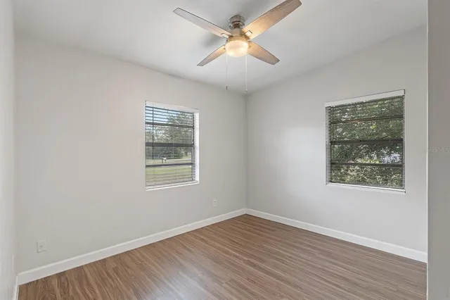 an empty room with wooden floor ceiling fan and windows
