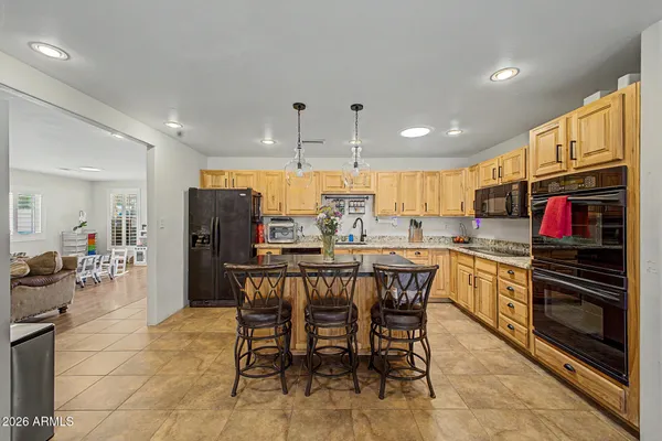 a kitchen with stainless steel appliances kitchen island granite countertop a refrigerator a stove a sink a dining table and chairs with wooden floor