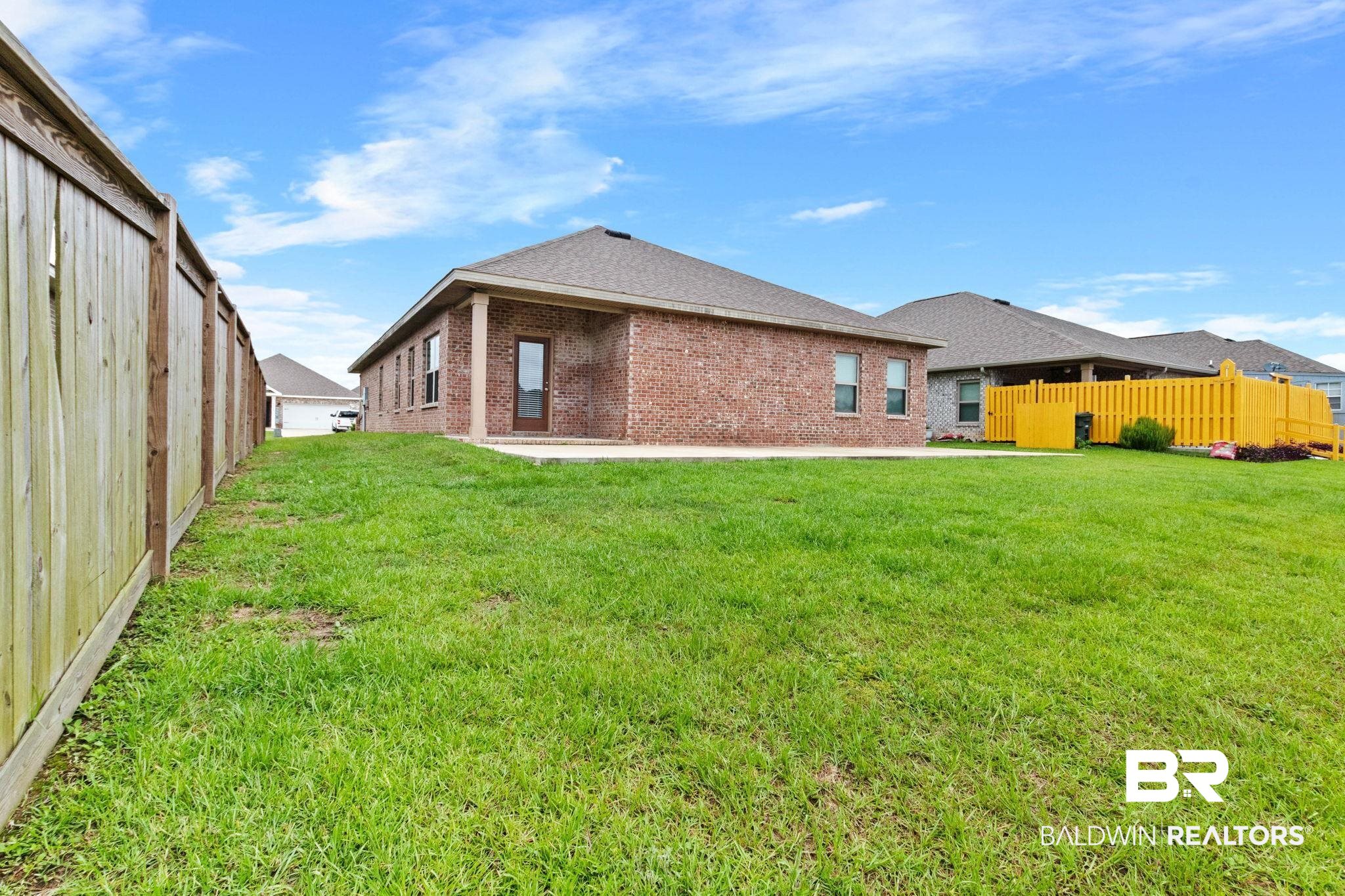 1710 Grouse Street Foley, AL 36535 - Photo 62 of 76 Expansive backyard featuring a brick exterior, covered patio, wood fencing, and a vibrant yellow picket fence