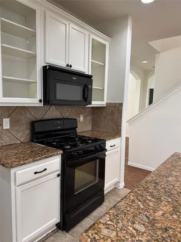 a kitchen with granite countertop white cabinets and black appliances