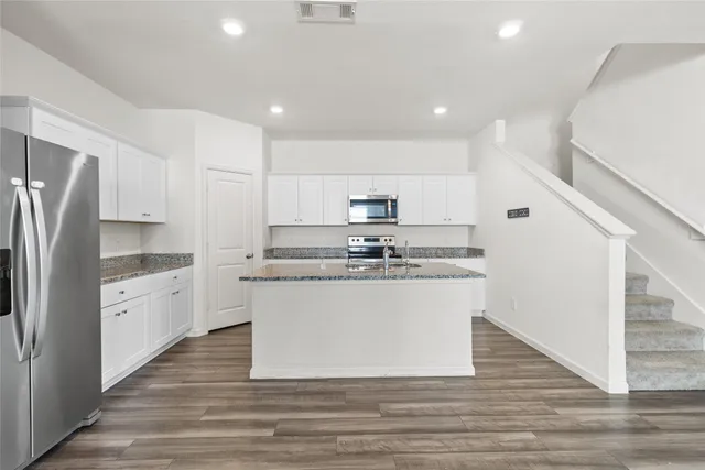 a large kitchen with stainless steel appliances granite countertop a large stove a refrigerator a sink and white cabinets with wooden floor