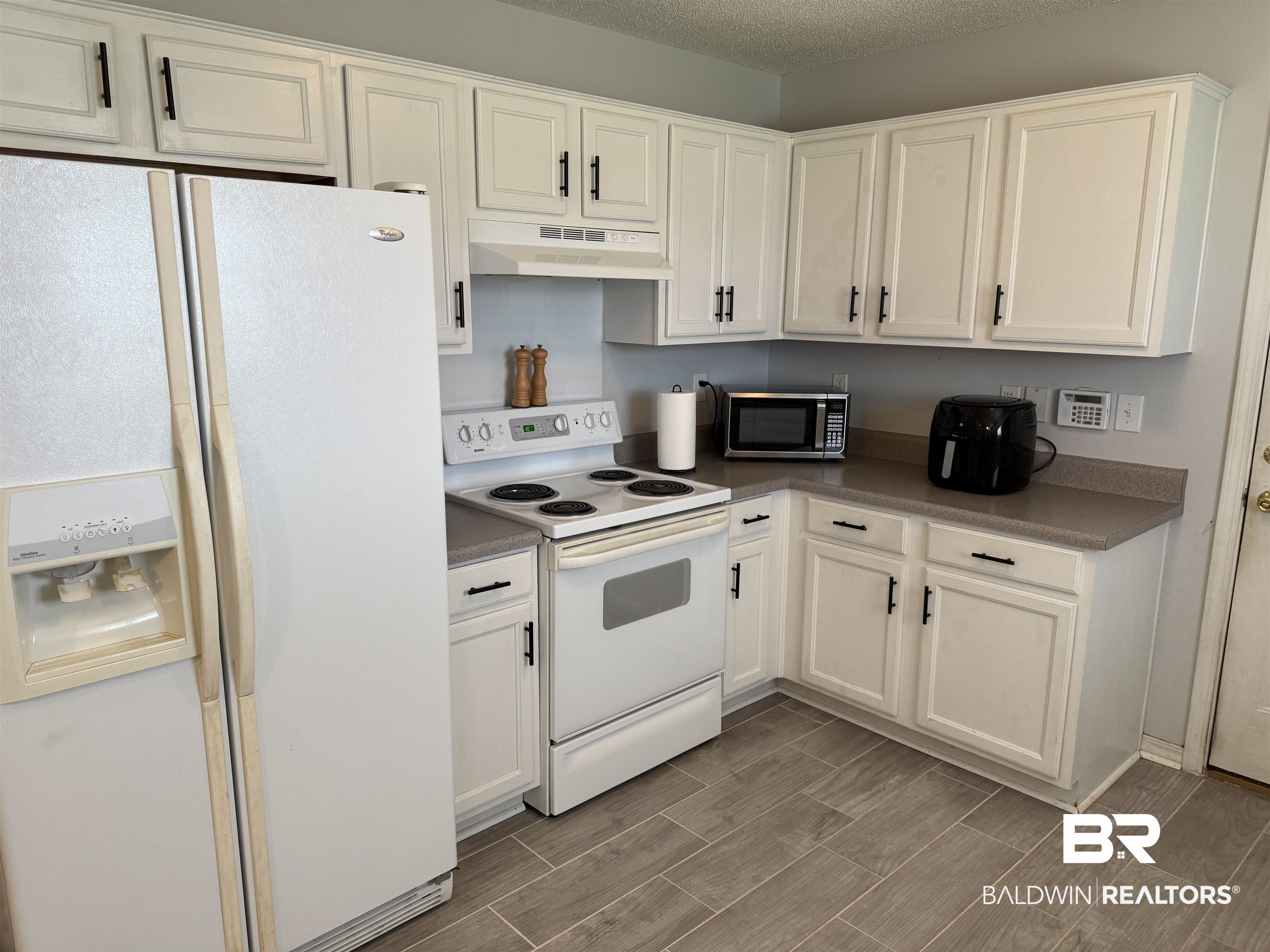 12932 Hopper Road Summerdale, AL 36580 - Photo 2 of 18 Kitchen with white appliances, under cabinet range hood, dark countertops, white cabinets, and a textured ceiling