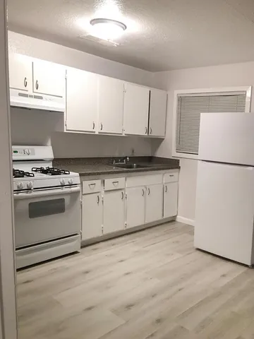a kitchen with granite countertop a sink a stove a refrigerator and white cabinets