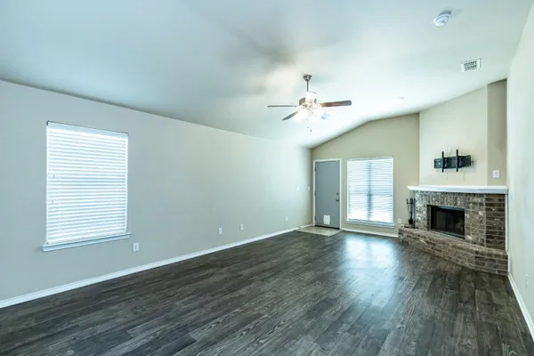 an empty room with wooden floor fireplace and windows