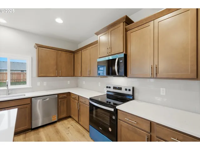 a kitchen with stainless steel appliances a sink dishwasher a stove top oven a refrigerator with wooden cabinets and floor