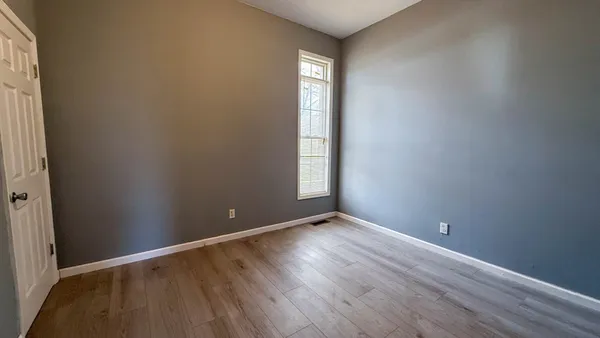 a view of an empty room with wooden floor and window