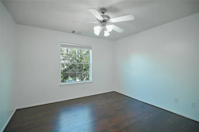 an empty room with wooden floor chandelier fan and windows