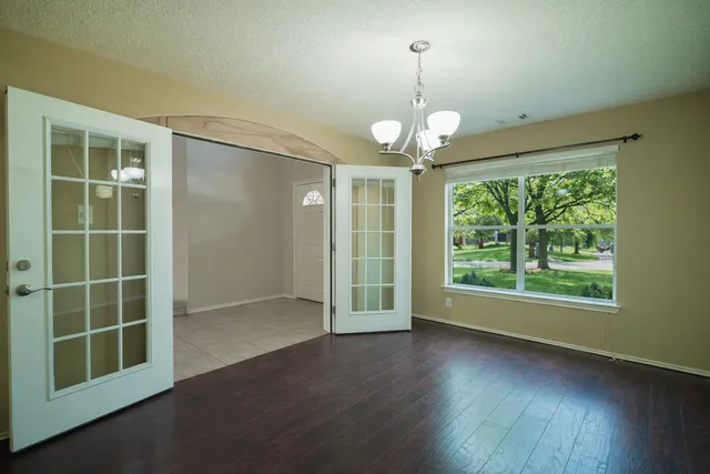 an empty room with wooden floor chandelier and glass door