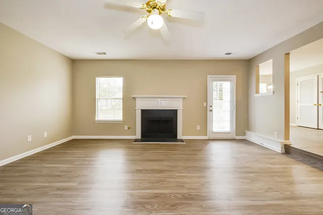 an empty room with wooden floor fireplace and windows