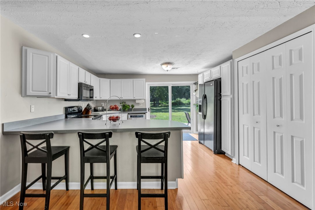 2264 Acre Road Akron, OH 44320 - Photo 10 of 47 Kitchen with a peninsula, light wood finished floors, a textured ceiling, black appliances, and a kitchen breakfast bar