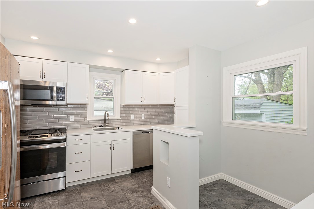 3719 Walter Road North Olmsted, OH 44070 - Photo 11 of 35 Renovated kitchen featuring white cabinetry, stainless steel appliances, grey subway tile backsplash, and light-toned countertops