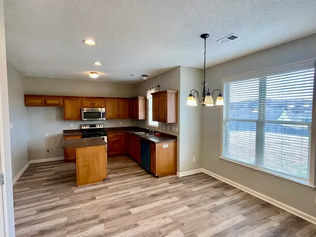 a kitchen with stainless steel appliances kitchen island granite countertop a stove top oven a sink dishwasher a refrigerator and a dining table with wooden floor
