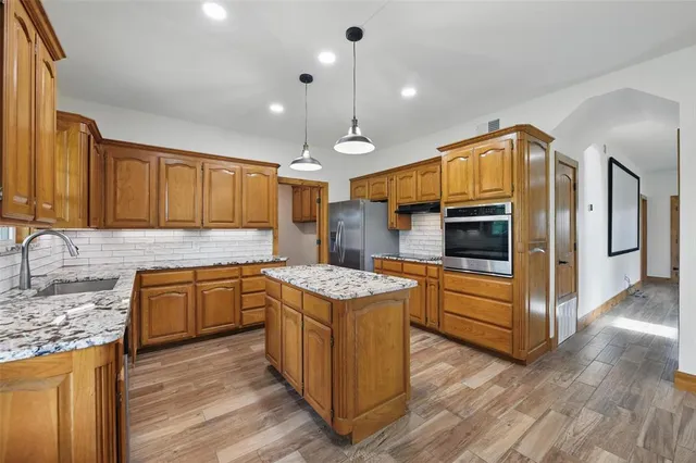 a kitchen with stainless steel appliances granite countertop a sink a stove top oven a refrigerator with wooden floors