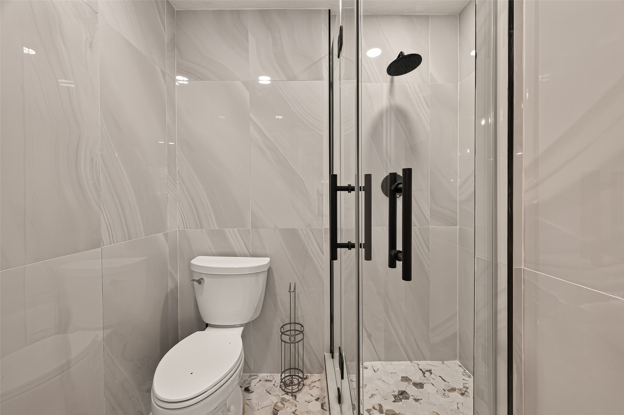 16619 Tibet Road Friendswood, TX 77546 - Photo 14 of 29 Modern bathroom featuring sleek, large-format tiles, a glass-enclosed shower with black fixtures, and a contemporary toilet. The space is well-lit and elegant, offering a clean, sophisticated look.