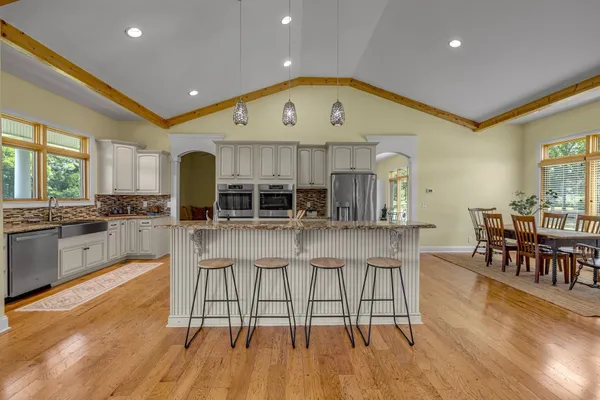 a kitchen with stainless steel appliances granite countertop a refrigerator a stove top oven and a dining table with wooden floor