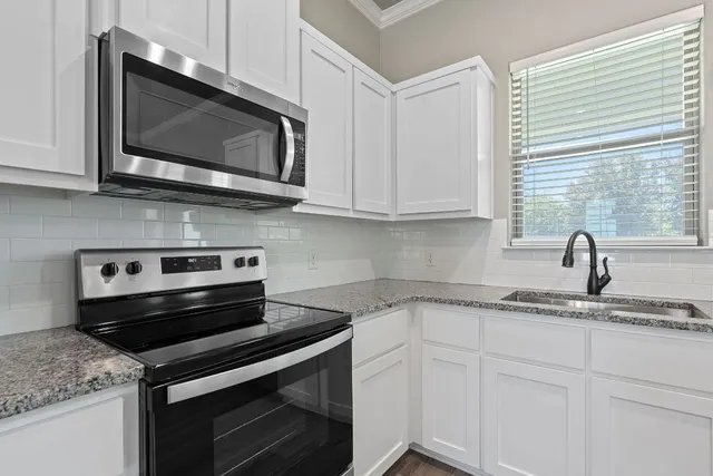 a kitchen with stainless steel appliances granite countertop white cabinets and a stove top oven