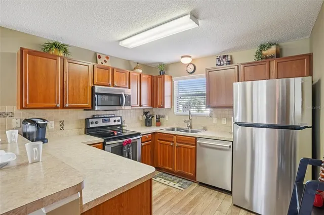 a kitchen with stainless steel appliances granite countertop a refrigerator a sink dishwasher a stove top oven a refrigerator with wooden floor and cabinets