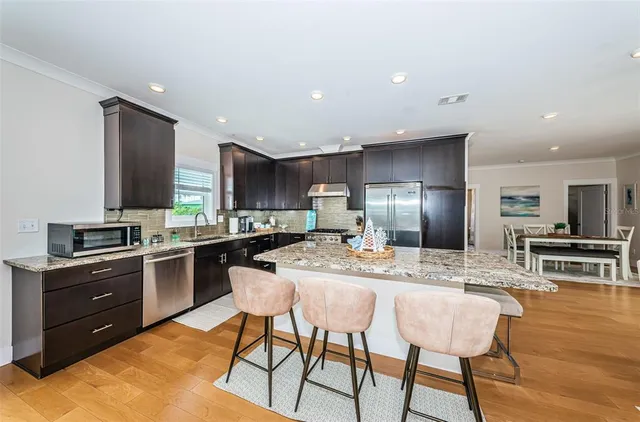 a kitchen with stainless steel appliances granite countertop a stove top oven a sink dishwasher and a refrigerator with wooden floor