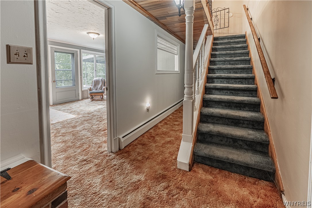 6775 Bear Ridge Road Pendleton, NY 14094 - Photo 26 of 48 Carpeted stairs ascend alongside a hallway with wood-paneled ceiling details.